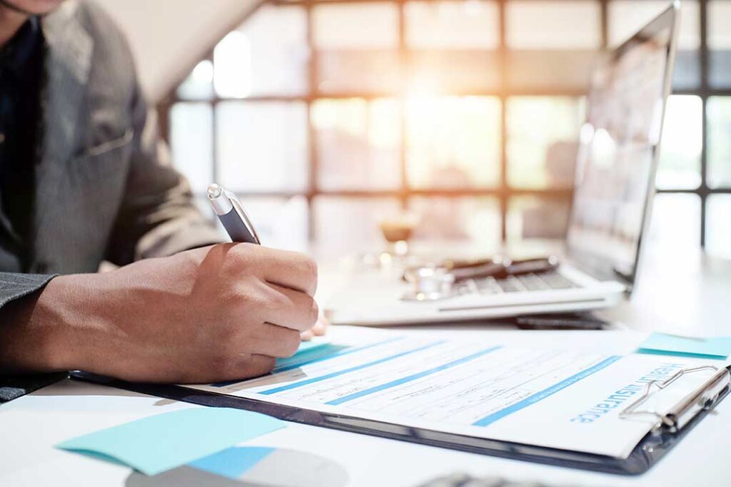 A couple reviews liability insurance documents at a kitchen table beside a laptop and car keys.