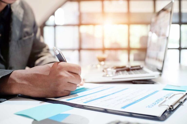 A couple reviews liability insurance documents at a kitchen table beside a laptop and car keys.